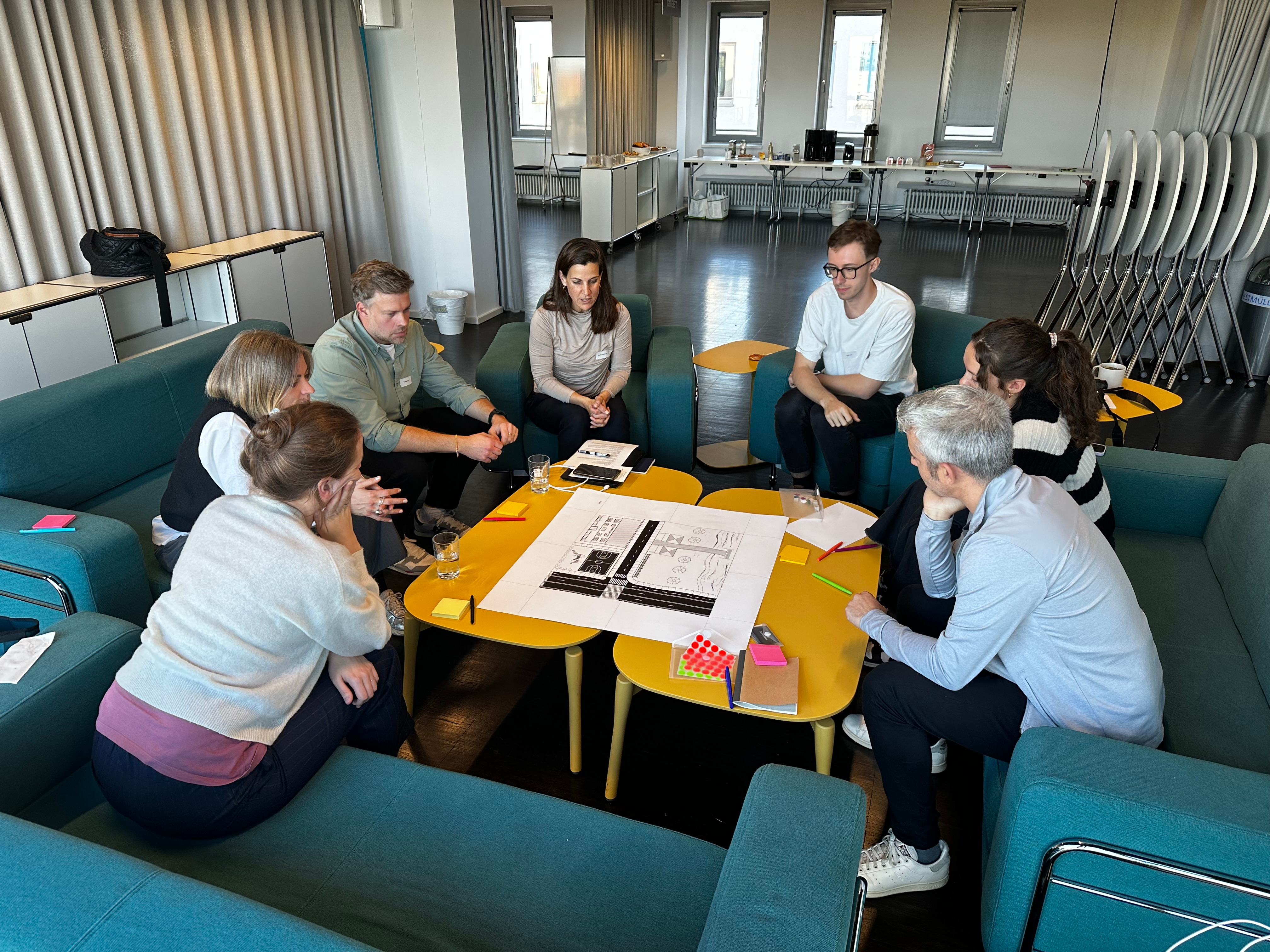 7 people in a workshop, sitting around an example map on a table. Everyone has some pens, notebooks and post-its.